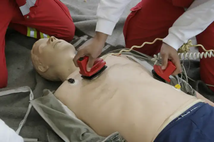 Rettungsassistent demonstriert an einer Rettungspuppe die Anwendung eines Defibrillators