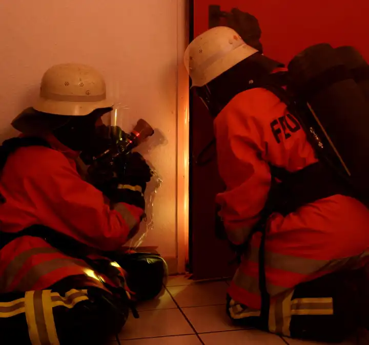 Two firemen with breathing protection at a practice of opening a door in a building