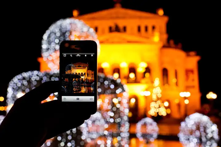 Tourist macht Handy-Foto von der Alten Oper und ihrer Weihnachtsdekoration in Frankfurt am Main.
