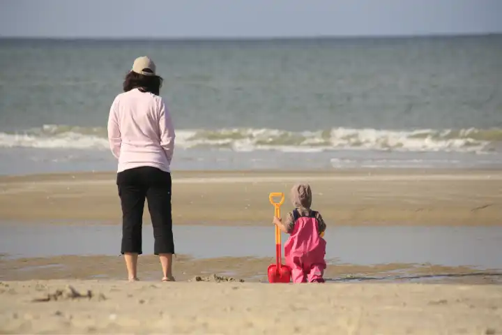 Frau und Kind mit Schaufel schauen aufs Meer