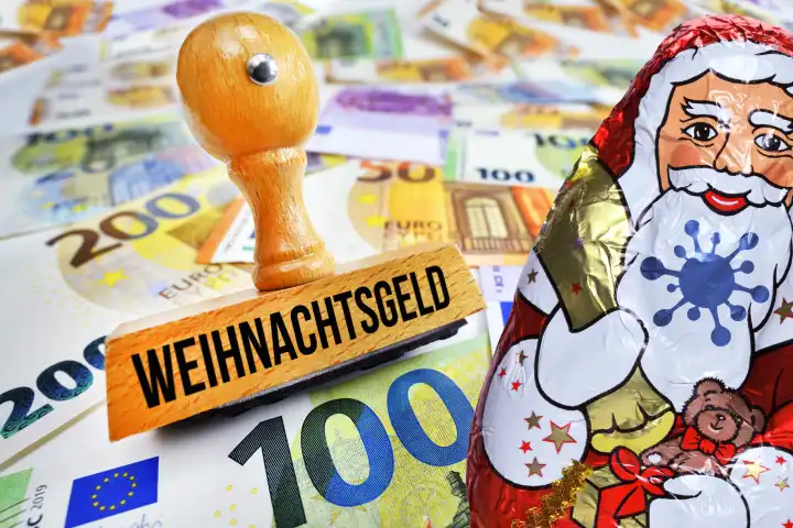 Stempel mit Aufschrift Weihnachtsgeld und Schokoladen-Weihnachtsmann mit Corona-Symbol auf Geldscheinen