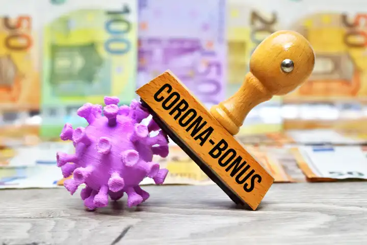 Stempel mit Aufschrift Corona-Bonus und Coronavirus-Modell vor Geldscheinen