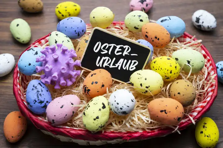 Easter eggs and corona model in an Easter nest, German words for Easter holiday on a board