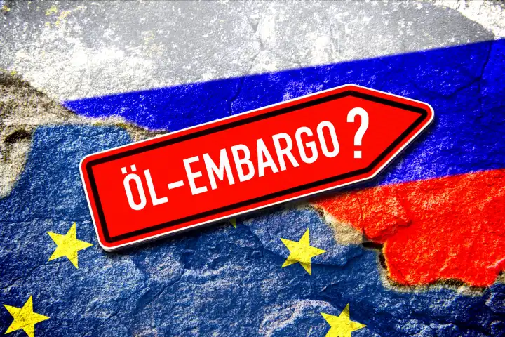 Schild mit der Aufschrift Öl-Embargo vor den Fahnen von EU und Russland