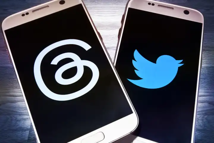 Auf einem Tisch liegen Smartphones mit den Logos von Threads und Twitter, neuer Kurznachrichtendienst Threads will Twitter Konkurrenz machen