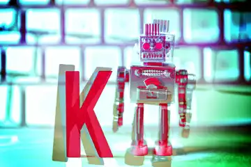Buchstabe K und Roboterfigur als I vor einer Computertastatur, Symbolfoto künstliche Intelligenz, Fotomontage