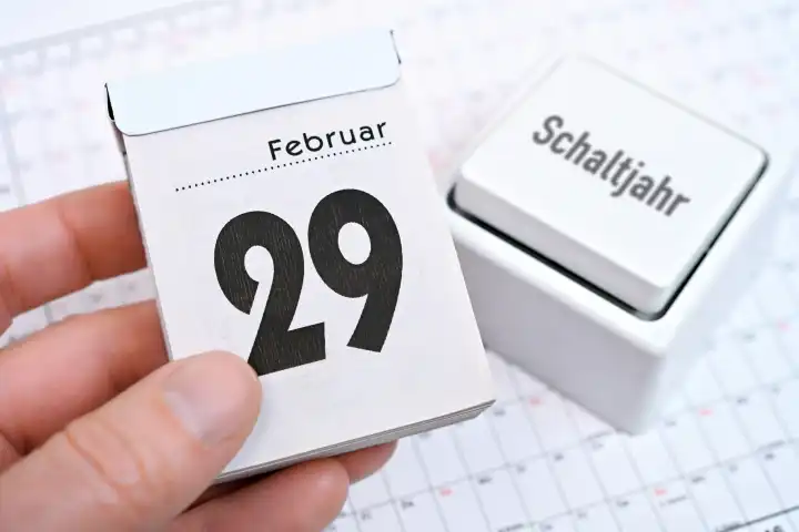 Hand holds calendar sheet of February 29 in front of a switch with inscription leap year, photomontage
