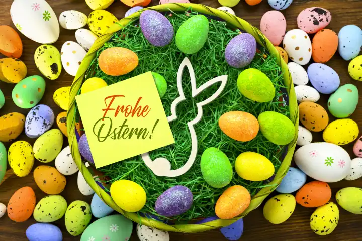 Osterhasenfigur und bunte Ostereier mit Zettel und Aufschrift Frohe Ostern in einem Osternest, Fotomontage