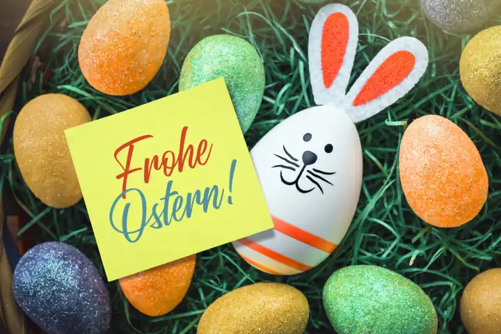 Osterhasen-Osterei und Zettel mit Aufschrift Frohe Ostern in einem Osternest, Fotomontage