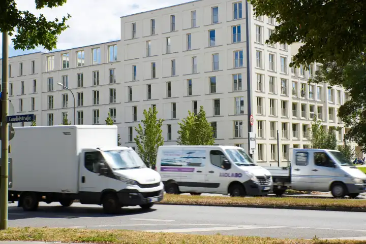Traffic middle ring / Candidstraße. Three staggered white panel vans, street sign visible. In the background, a new apartment block.