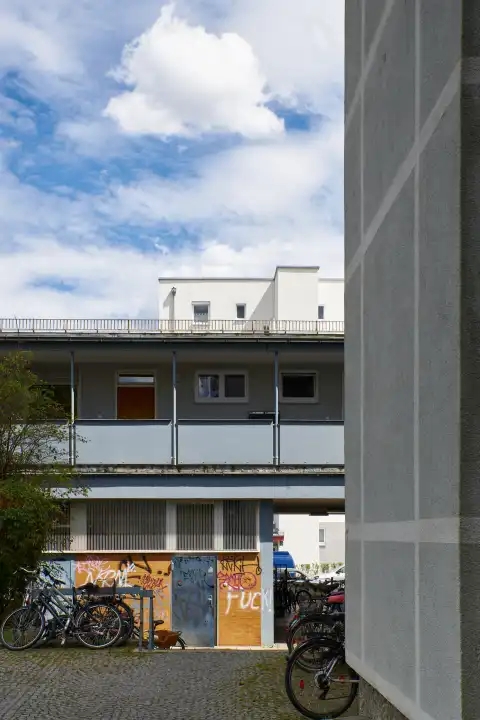 Backyard scene Untergiesing. 1 story cross building, with bicycles and graffity in the background 2020 redeveloped apartment block.