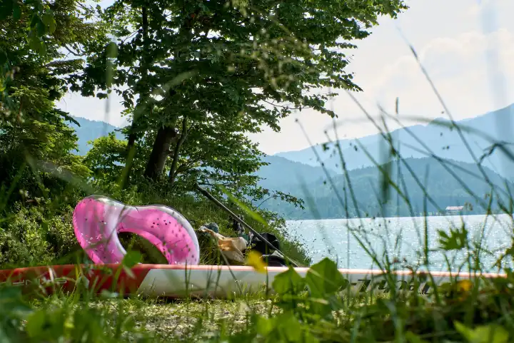 Walchensee. Badestelle mit pinkfarbenem Herz, SUP Board, Bierflaschen, Badeutensilien. Blick auf Westufer und Berge.