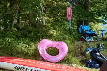 Walchensee. Bathing spot with pink heart, SUP board, beer bottles, bathing utensils, paddle, camping chair, wetsuit on the tree.