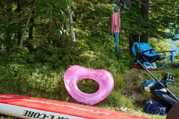 Walchensee. Badestelle mit pinkfarbenem Herz, SUP Board, Bierflaschen, Badeutensilien, Paddel, Campingstuhl, Neoprenanzug am Baum.