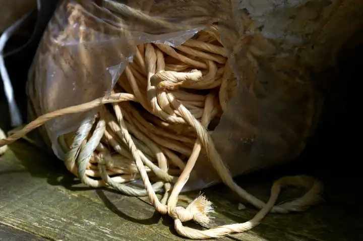 Ein großes Bündel Nylonschnur, verpackt in einer aufgerissenen Plastiktüte, auf einem Holzboden liegend.