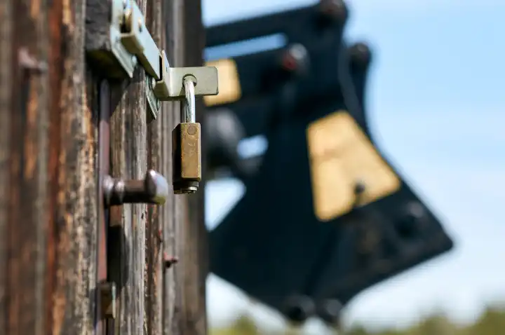 Padlock on the old wooden door with metal bolt. The door belongs to a wooden shed.  In the background, out of focus, a construction machine.