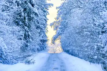 Light at the end of the road, winter-snow-covered highway through the forest after the onset of winter on the Swabian Alb, Münsingen, Baden-Württemberg, Germany.