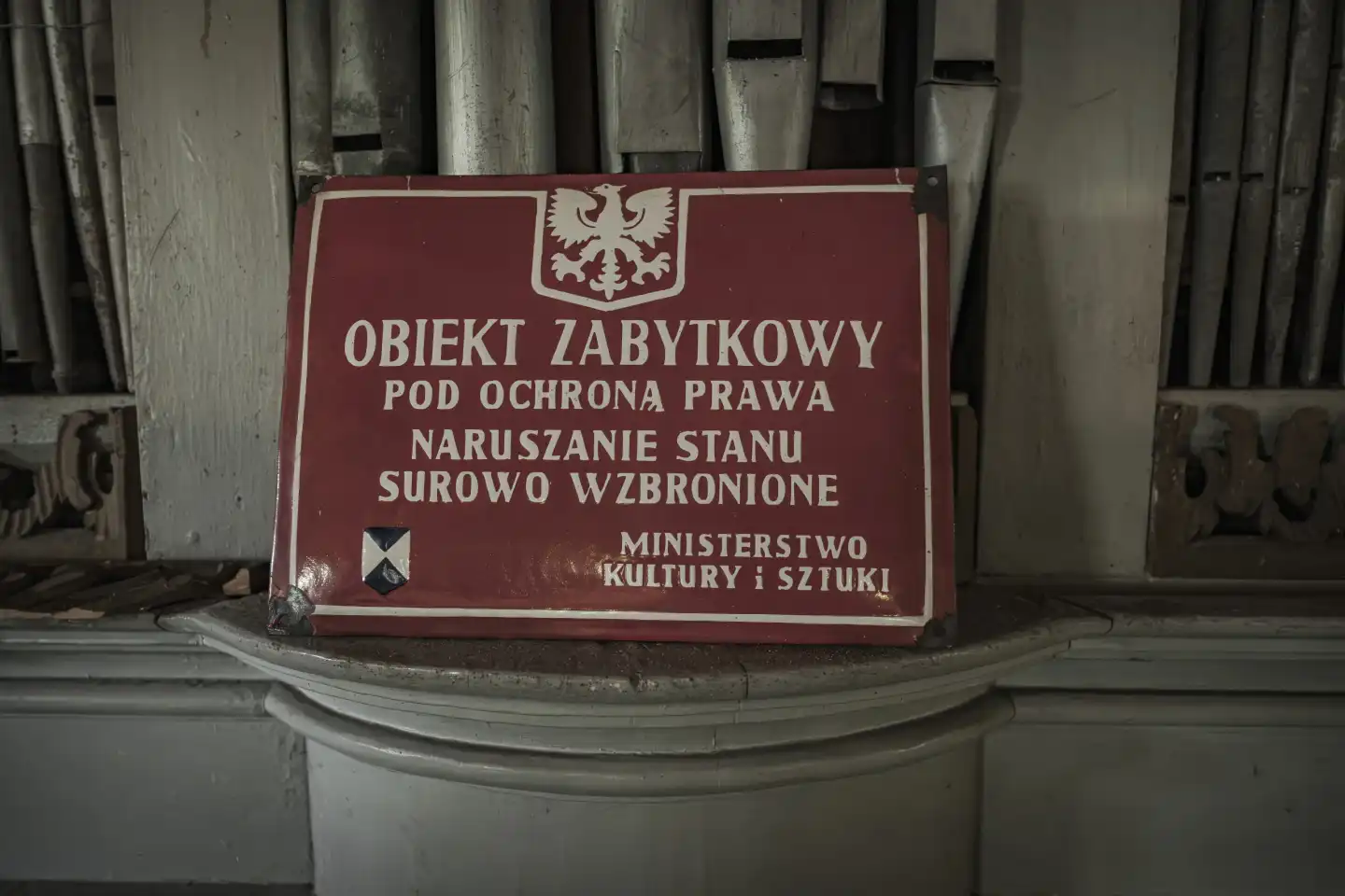 Blechschild mit weißer Schrift in Polnisch auf rotem Untergrund mit der Aussage des Ministeriums für Kultur und Kunst, dass das geschützte Denkmal unter dem Schutz des Gesetzes steht und dessen Verletzung streng verboten sind.