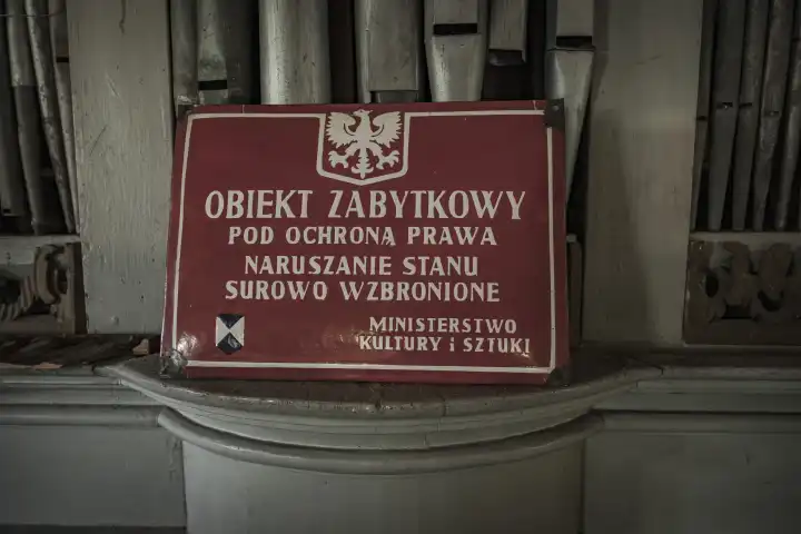 Metal sign with white writing in Polish on a red background with the statement of the Ministry of Culture and Art that the protected monument is under the protection of the law and its violation is strictly prohibited.