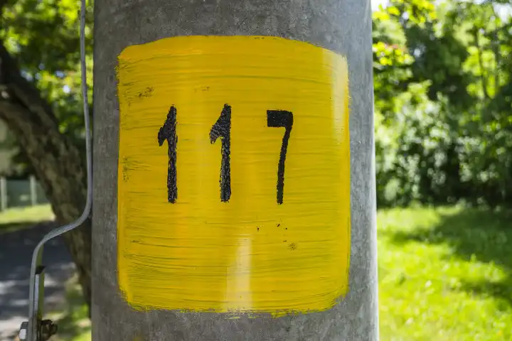 Zahl 117, Einhundertsiebzehn, aufgemalt Schwarz auf Gelb an einem Masten.
