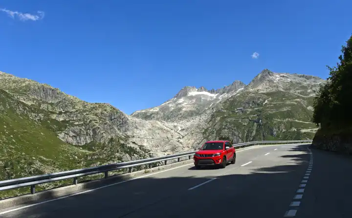 Red vehicle driving downhill on Furka Pass road towards Gletsch, Obergoms, Valais, Switzerland