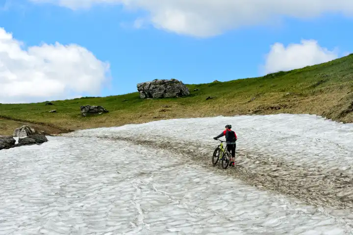 Mountainbiker schiebt sein Mountainbike über ein Schneefeld, Montriond, Chablais, Frankreich