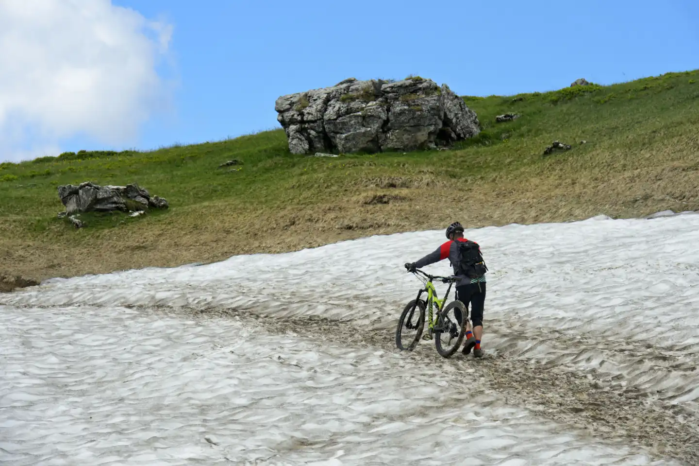 Mountainbiker schiebt sein Mountainbike über ein Schneefeld, Montriond, Chablais, Frankreich