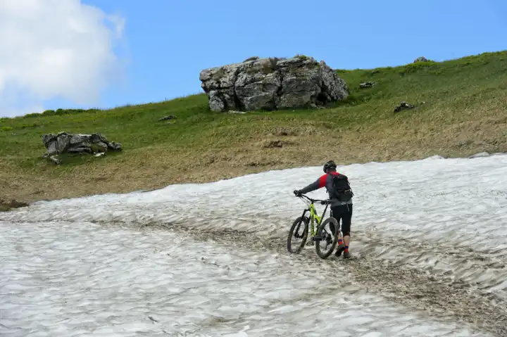 Mountain biker pushing his mountain bike over a snow field, Montriond, Chablais, France
