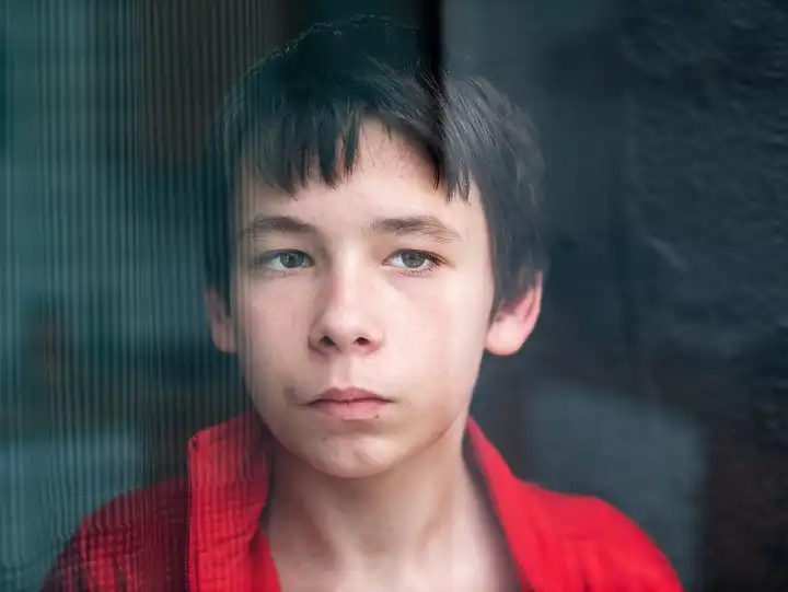 Portrait of a teenage boy at home looking through a window