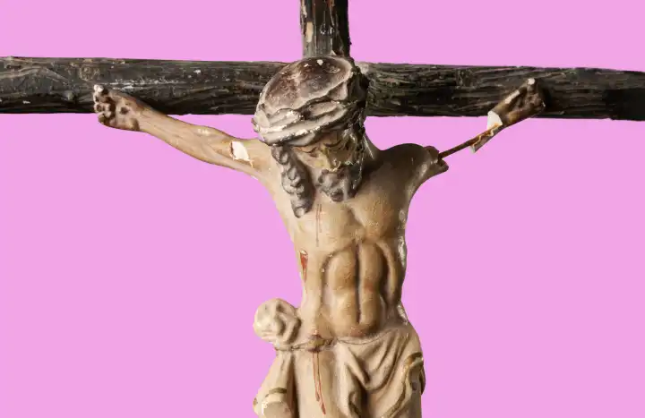 Zerbrochene und verstaubte Figur des gekreuzigten Jesus Christus vor pinkfarbenem Hintergrund