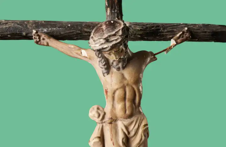 Zerbrochene und verstaubte Figur des gekreuzigten Jesus Christus vor grünem Hintergrund