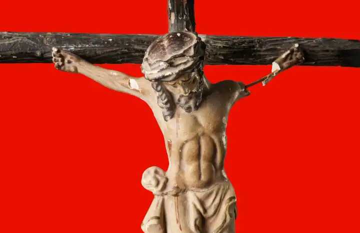 Zerbrochene und verstaubte Figur des gekreuzigten Jesus Christus vor rotem Hintergrund