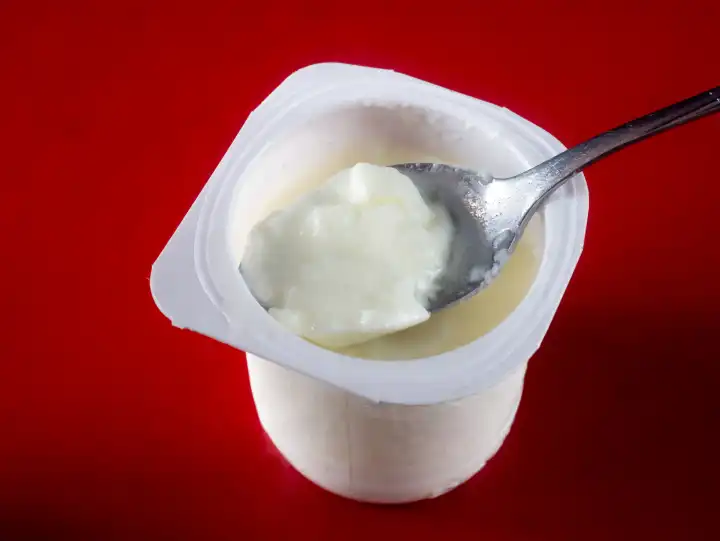 Yogurt cup with spoon against a red background