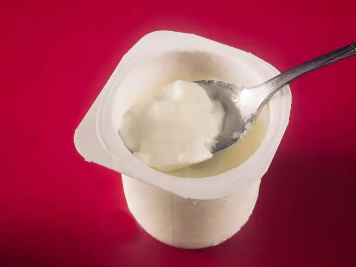 Yogurt cup with spoon against a red background