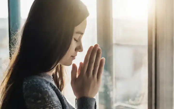 junge Frau betend am Fenster, KI generiert