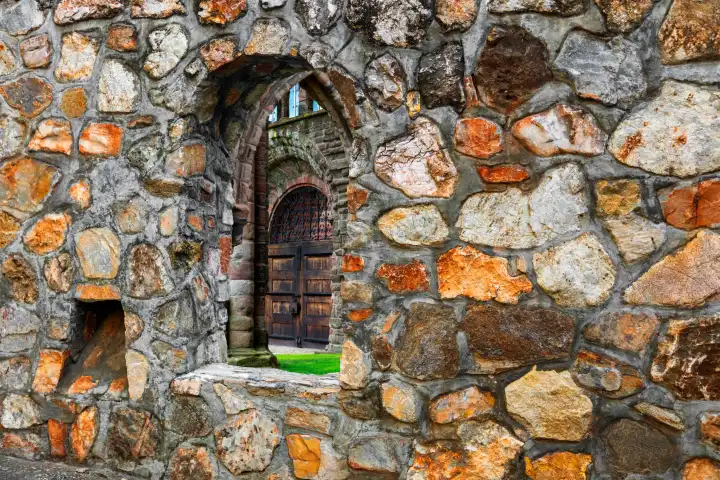 Blick durch ein Fenster einer historischen Mauer auf einene Kirchentüre