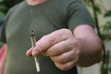 Ein Mann hält einen Joint zwischen den Fingern