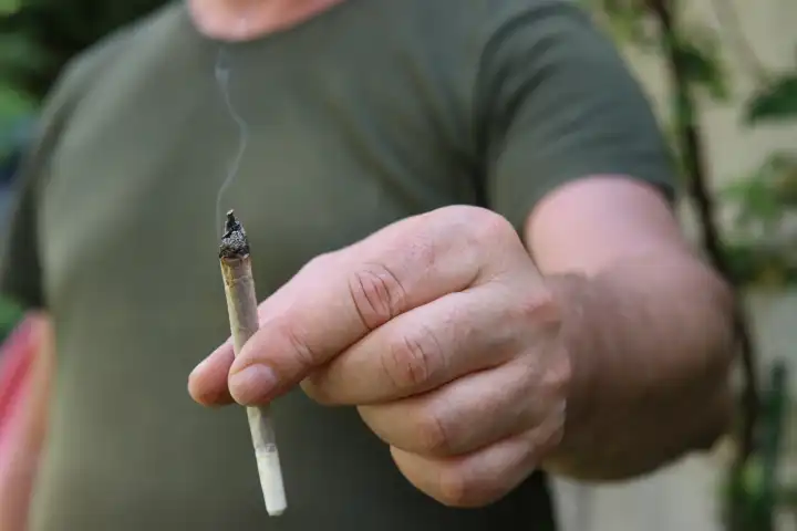 Ein Mann hält einen Joint zwischen den Fingern