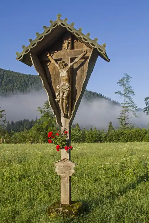 Idyllisches Wegkreuz auf einer Blumenwiese im Tal der Jachenau mit Bodennebel