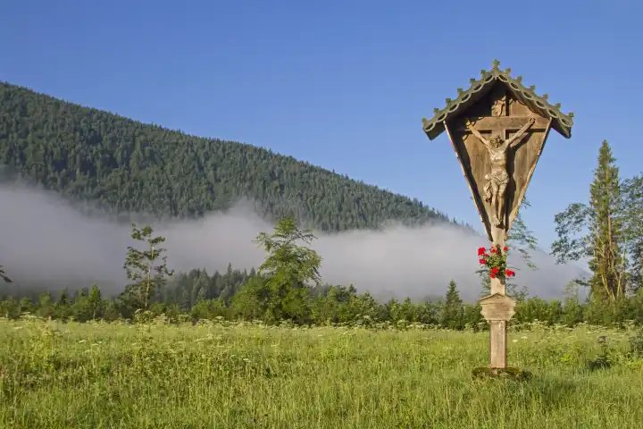 Idyllisches Wegkreuz auf einer Blumenwiese im Tal der Jachenau mit Bodennebel