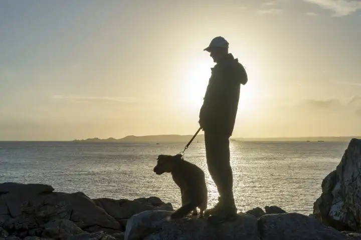 Mann mit Hund im Gegenlicht an der Küste