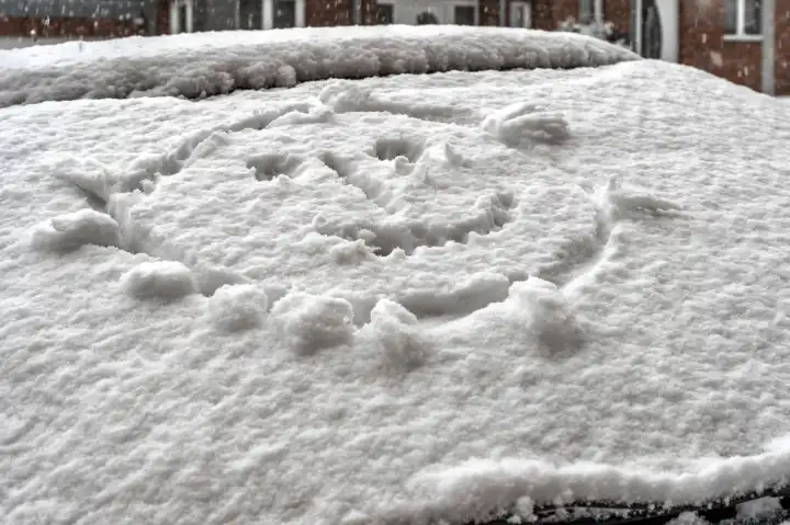 Smiley auf der schneebedeckten Heckscheibe eines PKW
