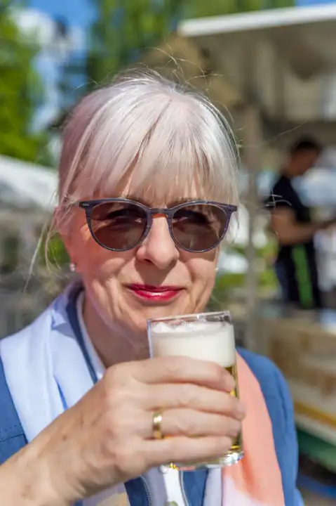 Senior woman with sunglasses and a beer glass, camera view, upright, Germany, North Rhine-Westphalia, Grevenbroich, public ground