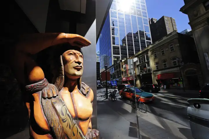 Geschnitzte Indianerfigur schaut auf das bunte Treiben der geschäftigen Yonge Street, Toronto, Kanada