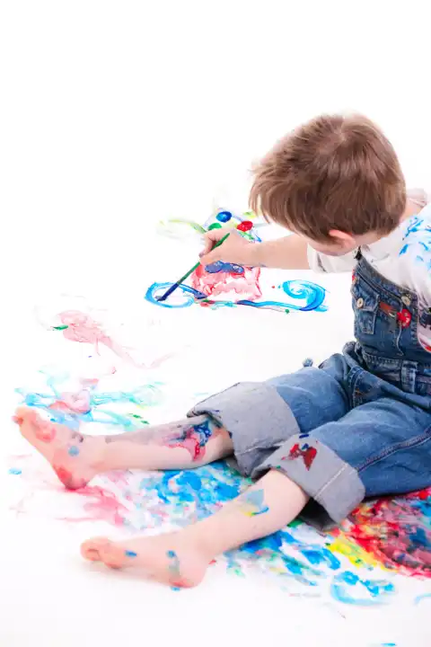 5 years old boy painting with finger paints on white background, focus on hand