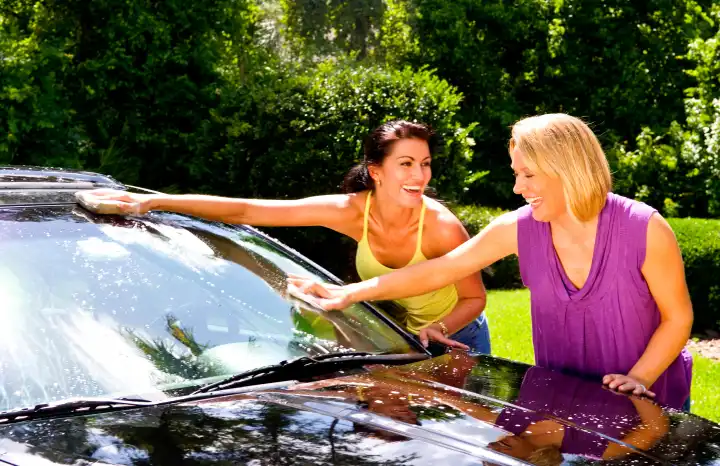 Girlfriends having fun washing car at home and relaxing together