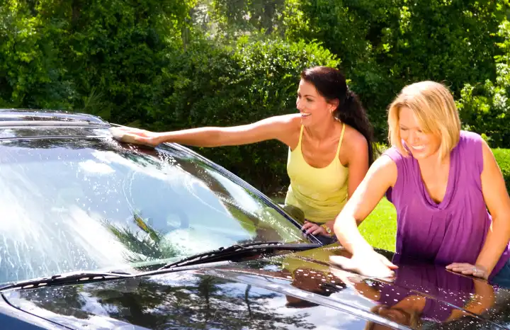 Girlfriends having fun washing car at home and relaxing together