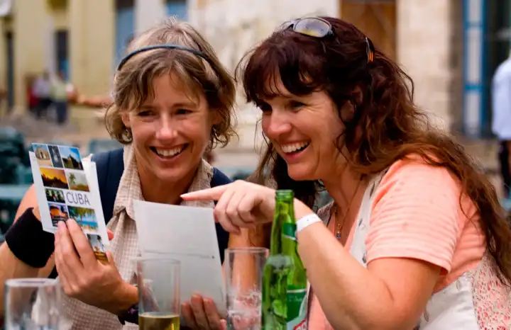 Tourist girl friends relax with drinks and look at postcards and have fun