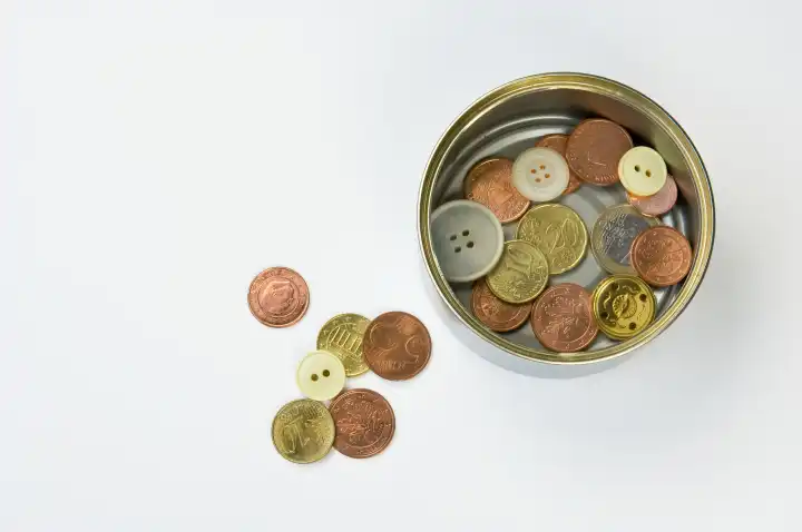 Konservendose mit Münzen und Knöpfen, einige liegen daneben