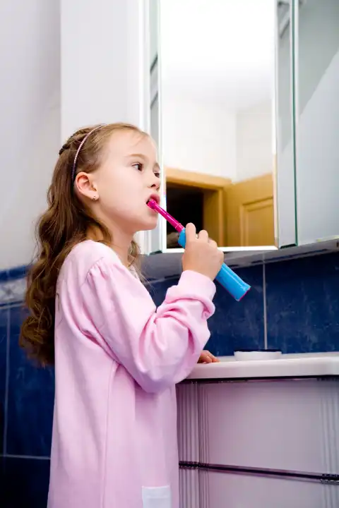 young girl brushing her teeth in front of mirror